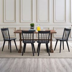 a dining room table with four chairs and a vase on the floor next to it