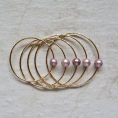 four gold rings with pink pearls on them sitting on a white surface next to each other