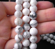 a person is holding some white and black marble beads in their hand while they are both wearing necklaces