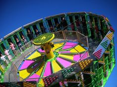 a colorful carnival ride with people standing on the top and one person in the background