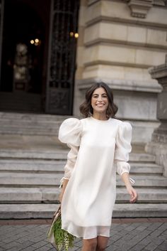 a woman is walking down the street wearing a white dress with puffy sleeves and heels