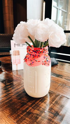 a mason jar filled with white flowers and sprinkles on a wooden table