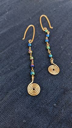 These simple and funky golden earrings are sure to catch an eye! The earrings start with a beautiful collection on oil slick blue and green glass beads, leading to a small golden wire spiral charm. They're great for a simple look with a touch of funky! Diy Wire Wrapped Earrings, Simple Handmade Earrings, Hammered Wire Earrings, Wire And Bead Earrings, Earring Design Ideas, Wire Jewelry Diy Tutorial, Simple Bead Earrings, Diy Earrings Dangle, Copper Wire Earrings