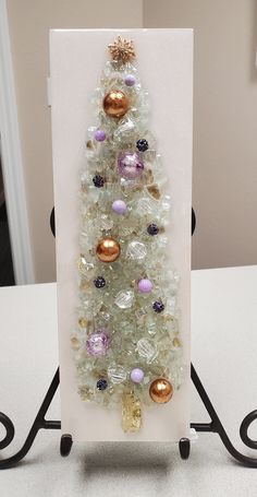 a small christmas tree made out of glass beads and other ornaments on a stand in front of a white wall