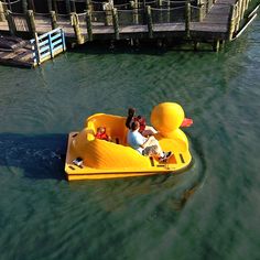 two people in a yellow rubber duck boat on the water next to a wooden dock