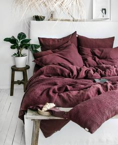 a bed with red sheets and pillows in a room next to a potted plant