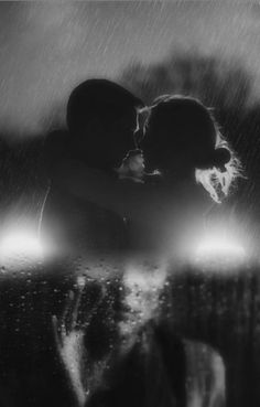 black and white photo of two people kissing under an umbrella in the rain at night