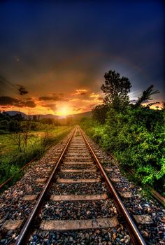 the sun is setting over an old railroad track