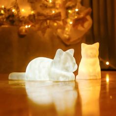 two white cat figurines sitting on top of a table next to a christmas tree