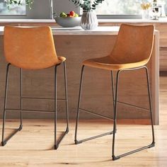 two brown chairs sitting on top of a wooden floor next to a kitchen countertop