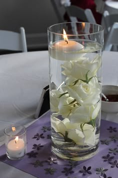 white flowers in a glass vase on a table with candles and napkins around it