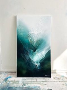 an abstract painting is displayed on the floor in front of a white wall with blue and green colors