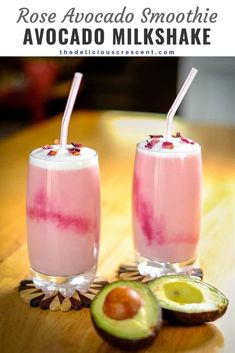 two glasses filled with fruit and drink on top of a wooden table next to an avocado