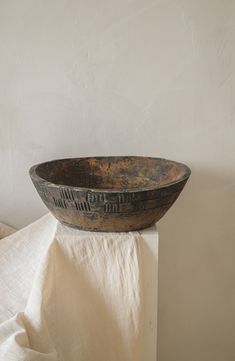 an old wooden bowl sitting on top of a white cloth covered table next to a wall