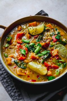 a bowl filled with soup and vegetables on top of a cloth next to a spoon