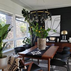 a dining room table with chairs and a potted plant in the center, next to a large window