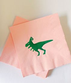 two pink napkins with a green dinosaur on them