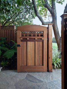 a wooden gate in the middle of a stone walkway next to a tree and shrubbery