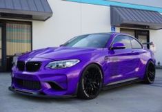 a purple car parked in front of a building with black rims and chrome wheels