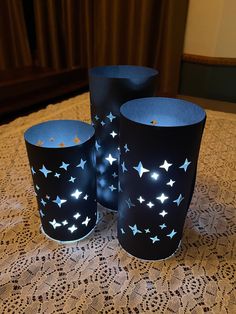 three blue cups with white stars on them sitting on a doily covered tablecloth