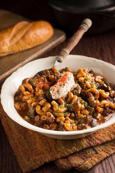 a white bowl filled with pasta and meat on top of a wooden table next to bread