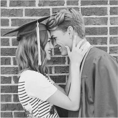 a man and woman hugging each other in front of a brick wall wearing caps and gowns