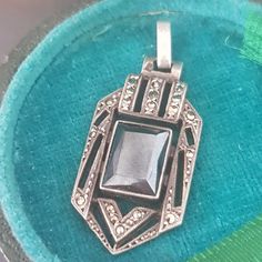 a silver pendant with a large stone in the center on a blue velvet cushioned surface