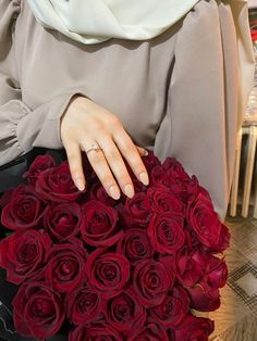 a woman in hijab holding a bouquet of red roses with her hand on it