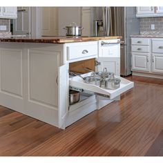 an open cabinet in the middle of a kitchen with white cabinets and wood flooring