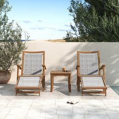 two wooden chairs sitting next to each other on a patio near a pool and trees