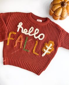 a red sweater with the words hello fall written on it next to some pumpkins