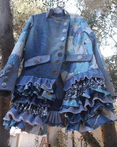 a blue jacket with ruffles and buttons hanging from a tree