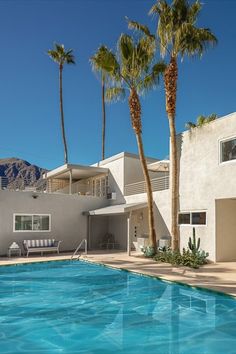 a large swimming pool next to a house with palm trees in front of it and mountains in the background