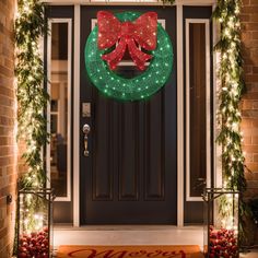 a christmas wreath on the front door of a house decorated with lights and garlands