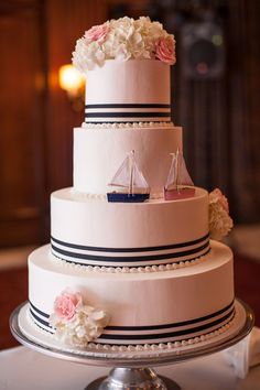 a three tiered wedding cake with flowers on the side and a sailboat on top