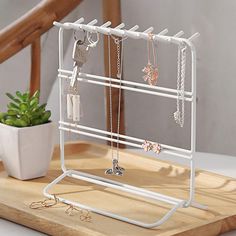 a white metal jewelry holder on top of a wooden table next to a potted plant