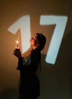 a woman holding a lit candle in front of a wall with the number seven drawn on it