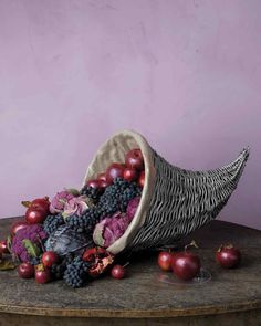 a basket filled with lots of fruit sitting on top of a wooden table next to a purple wall