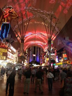 people are walking around in an indoor shopping mall at night with brightly lit signs on the ceiling