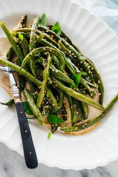 a white plate topped with green beans covered in sesame seeds and seasoning next to a fork