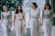 three women are walking down the street in white dresses and one is wearing a gray jacket