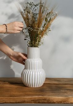 a person is arranging flowers in a white vase on a wooden table next to a wall