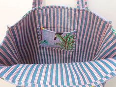 a blue and white striped bag hanging from a hook on a wall with an embroidered bird in the pocket