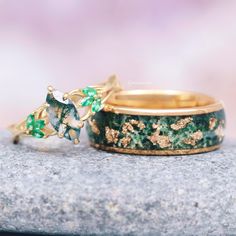 two rings with green and gold designs sitting on top of a stone slab next to each other