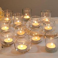 many lit candles in glass bowls on a table