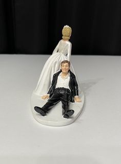 a bride and groom figurine sitting next to each other on a white surface