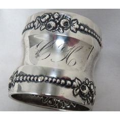 a close up of a silver ring with writing on the side and flowers around it