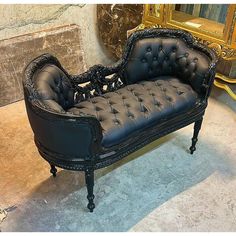 a black leather couch sitting on top of a floor next to a gold framed mirror