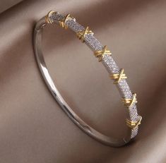 Elevate your style with our stunning Two-Tone Crystal Bangle Bracelet, an exquisite piece of jewelry that perfectly blends elegance and sophistication. This bracelet features a unique design with alternating bands of silver and gold, adorned with sparkling crystal accents that catch the light beautifully. The distinctive gold X details add a touch of modern charm, making this bangle a versatile accessory for any occasion. Crafted with high-quality materials, this bangle bracelet is both durable Unique Bracelets Gold, Silver Bangle Bracelets Unique Modern, Silver Bangle With Elegant Design For Gift, Modern Gold Jewelry Unique Designs, Modern Bangle, Necklace Chain Types, Modern Gold Jewelry, Jewelry Illustration, Crystal Bangle