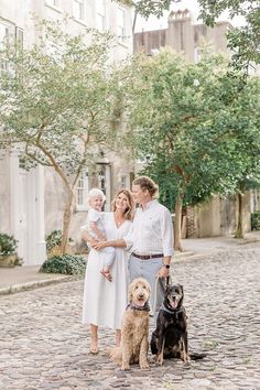 a family with two dogs posing for a photo in front of some trees and buildings